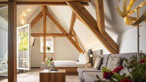 Ein gemütliches Schlafzimmer im Loft-Stil mit freiliegenden Holzbalken, einem Bett, einer Couch und einer modernen Lampe.