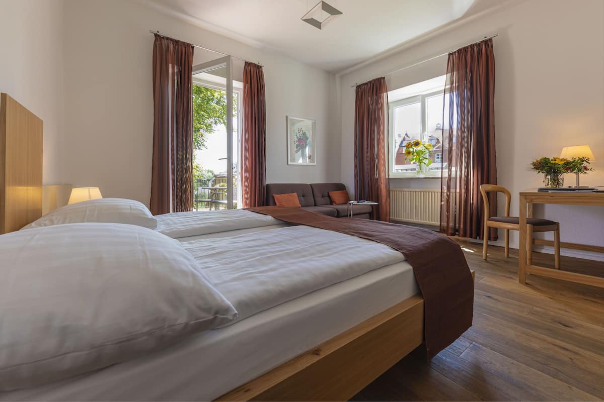 Habitación de hotel con una cama grande, un escritorio con lámpara y vistas al exterior.