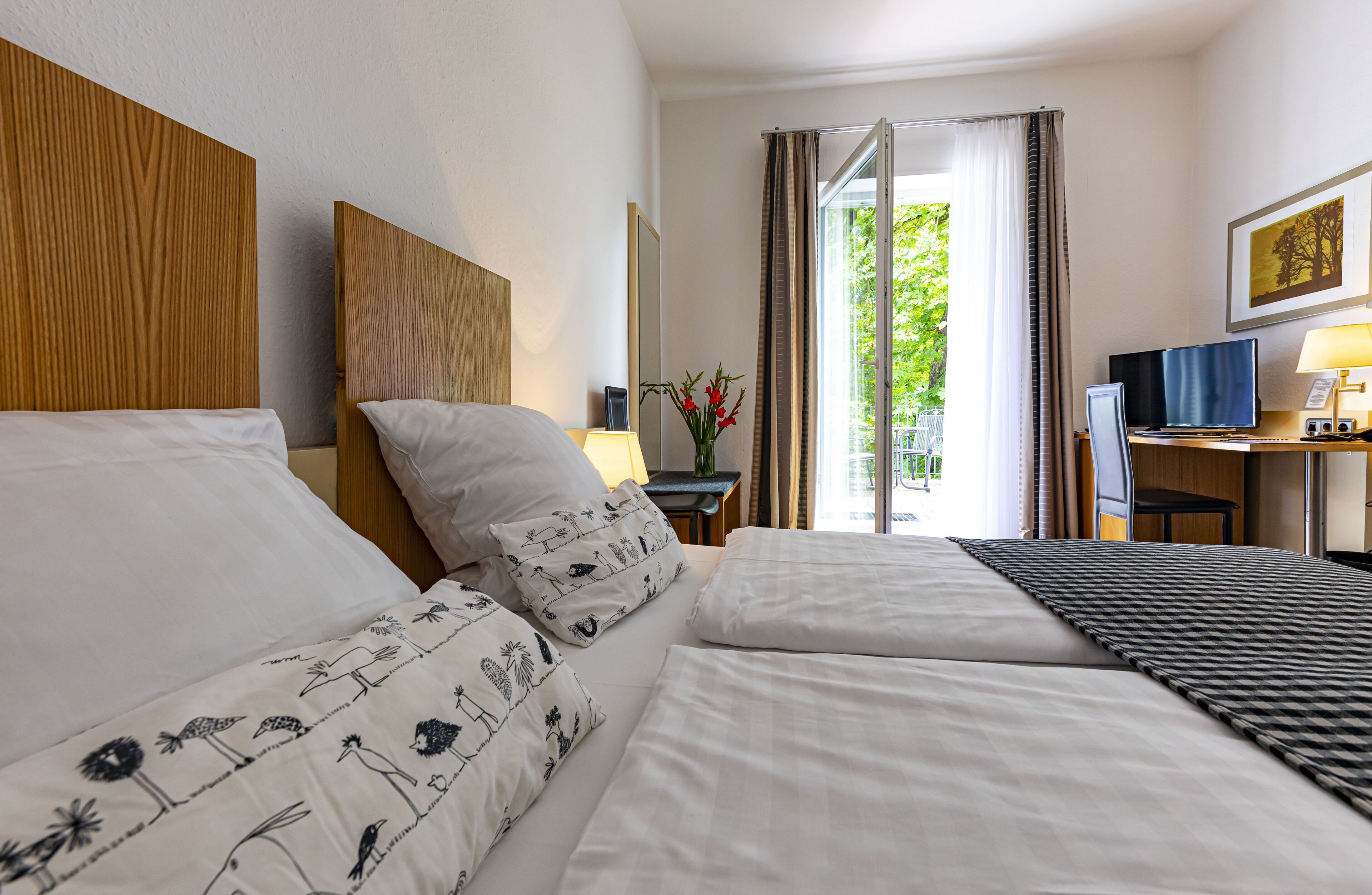 Habitación de hotel con dos camas, un escritorio, una silla, una lámpara y una ventana con cortinas.
