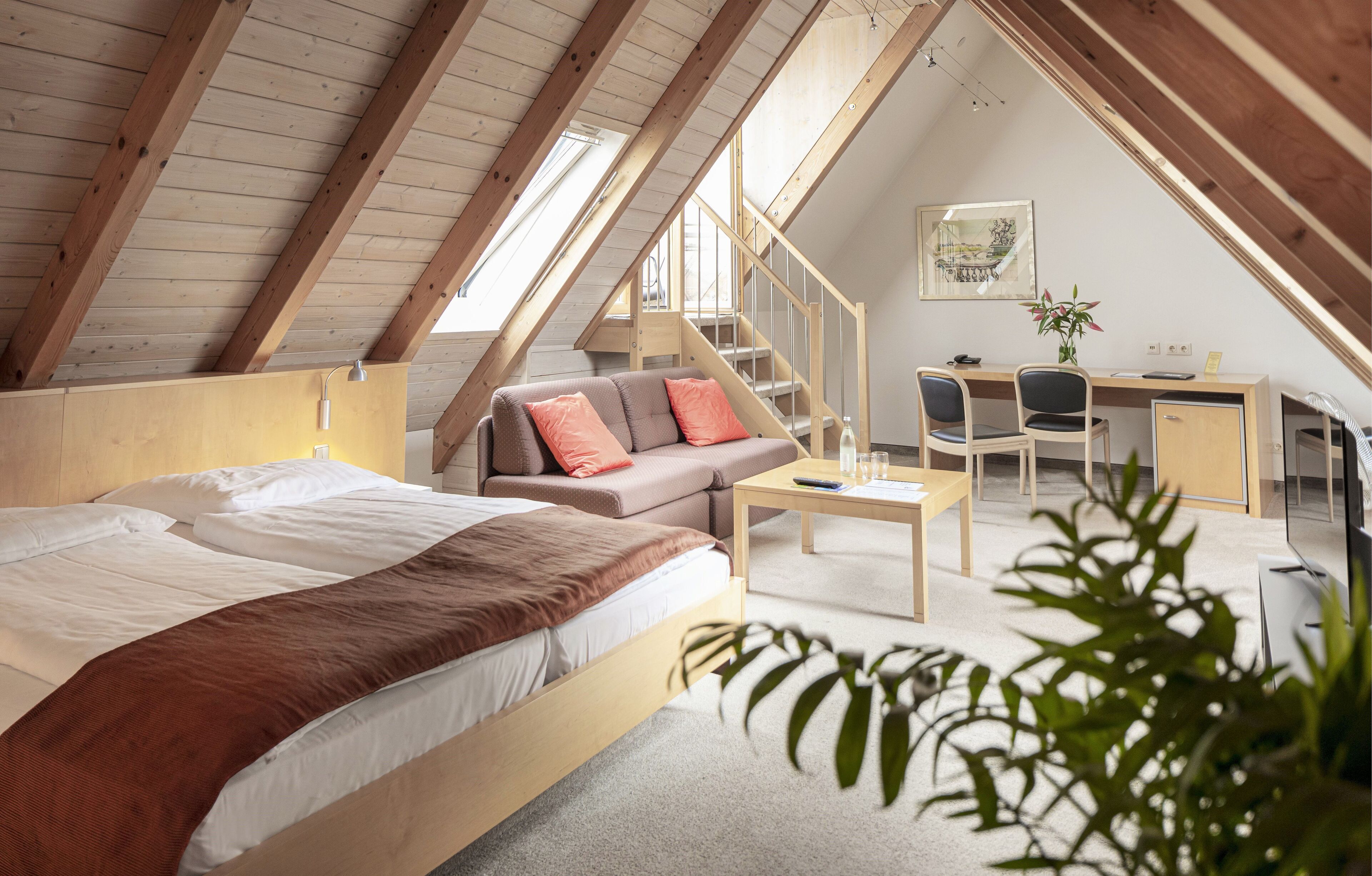 A cozy attic bedroom with a bed, a sofa, a desk, and a staircase.
