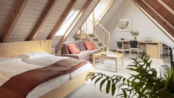 A cozy attic bedroom with a bed, a sofa, a desk, and a staircase.
