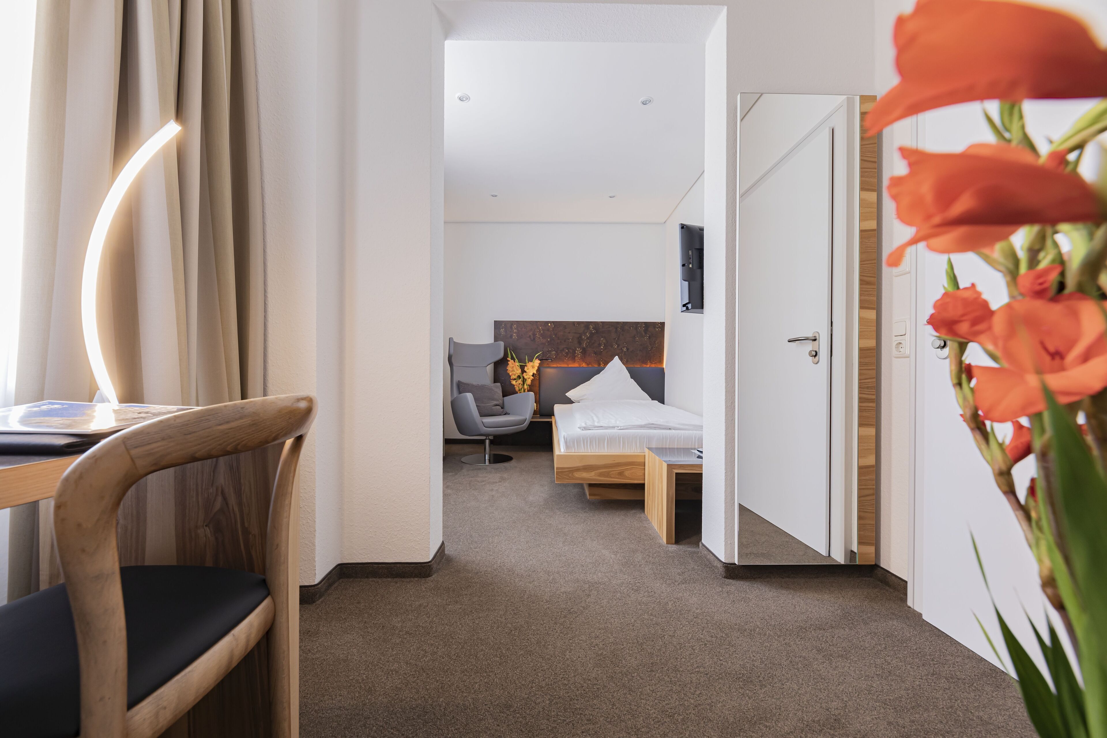 Una habitaci ón de hotel moderna con una silla de madera, un escritorio, una cama y un pequeño rincón de descanso con una silla y una mesa.
