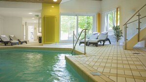 Ein Hallenbad mit Liegestühlen, gefliestem Boden und Blick auf Grünflächen.