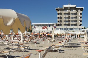 A beach with rows of sun loungers and umbrellas, a building with balconies, and a clear blue sky. - Hotel Ascot & Spa (Rimini)