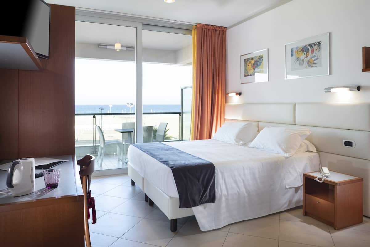 A hotel room with a bed, bedside table, and a view of the beach.