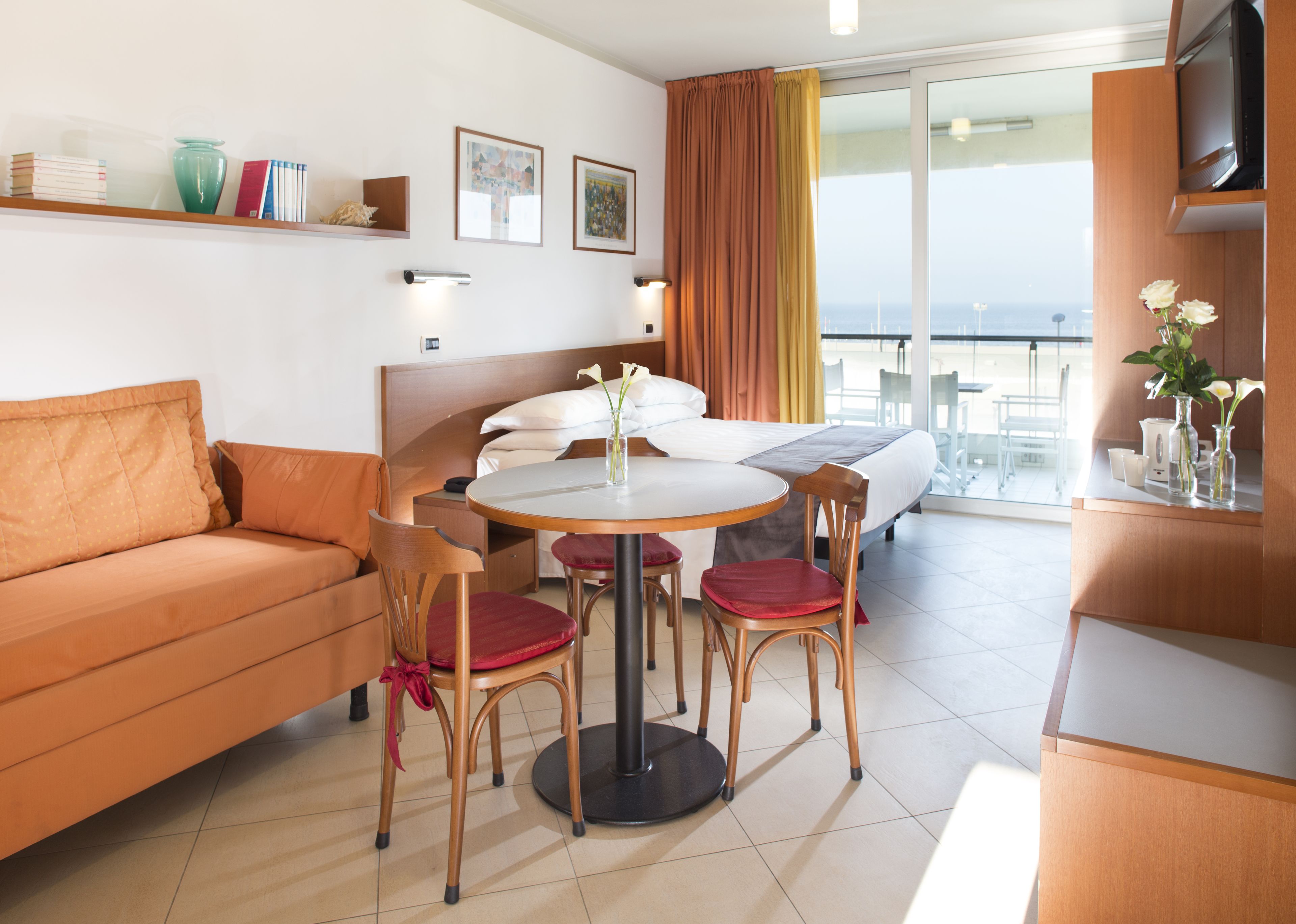 Una habitación de hotel con cama, sofá, mesa de comedor con sillas, televisor y balcón con vistas.
