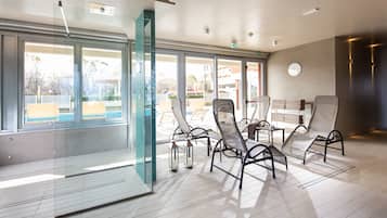 Un área de piscina interior moderna con paredes de vidrio, sillones de descanso y vistas al exterior.