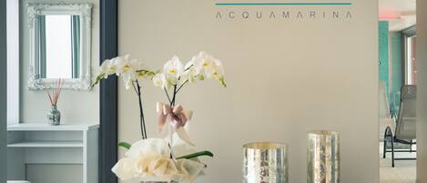 A reception area with a mirror, a vase with white flowers, and two metallic candle holders on a glass table.