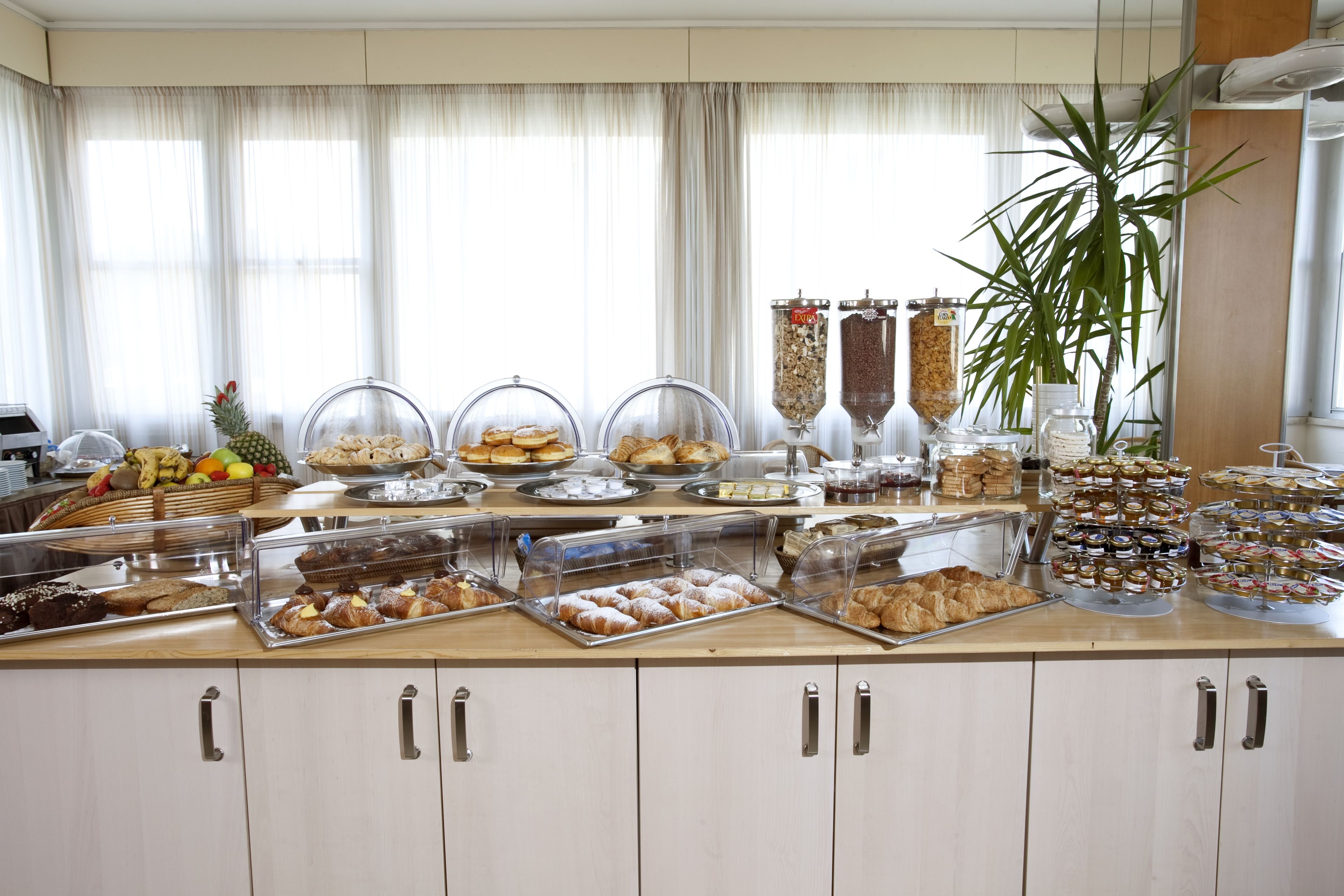 A buffet with various food items, including pastries and fruits, arranged on a counter with a large window in the background.