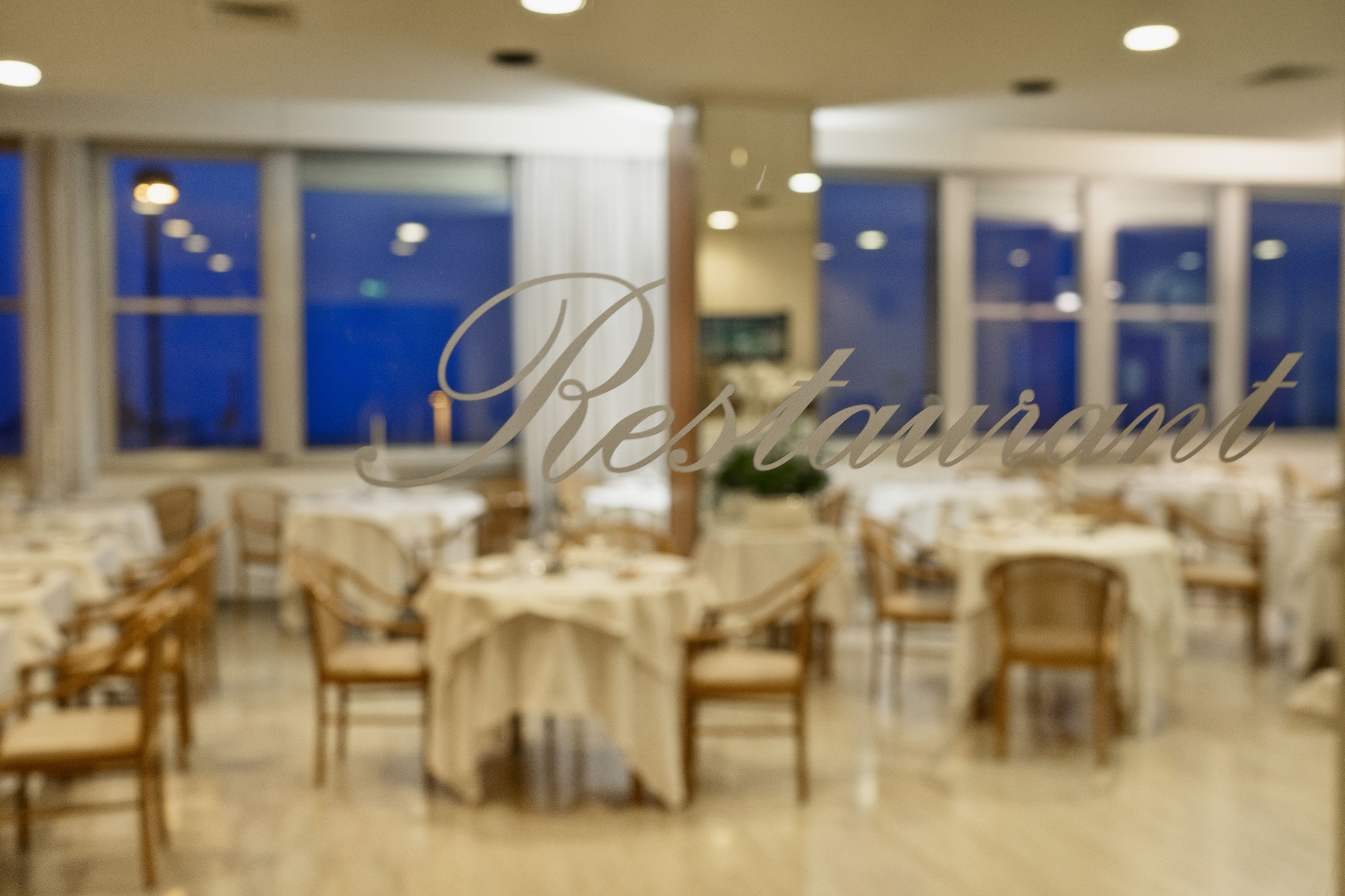 Um restaurante com várias mesas e cadeiras, grandes janelas e decoração de interiores moderna.