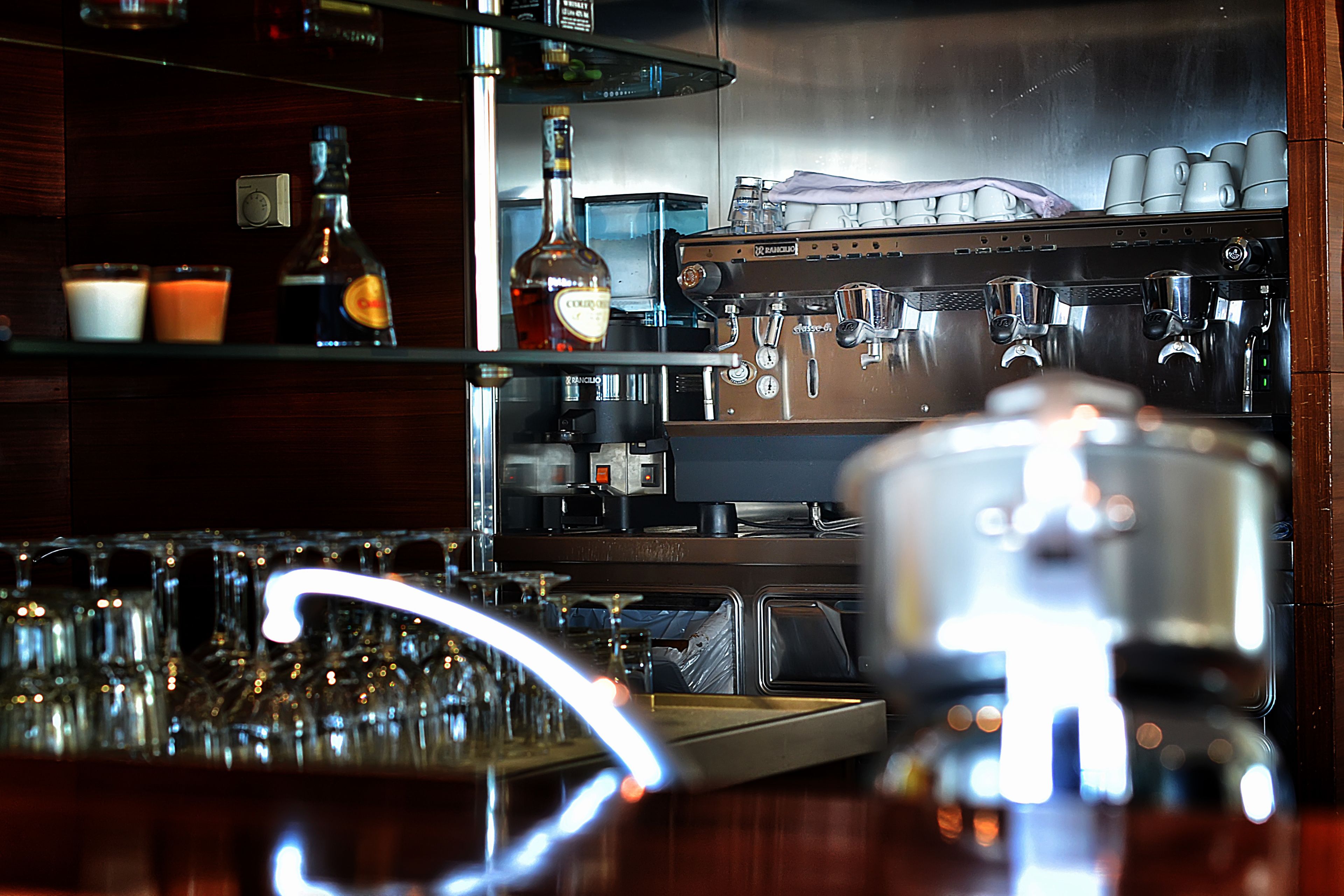A bar area with shelves of bottles, glasses, and a coffee machine.