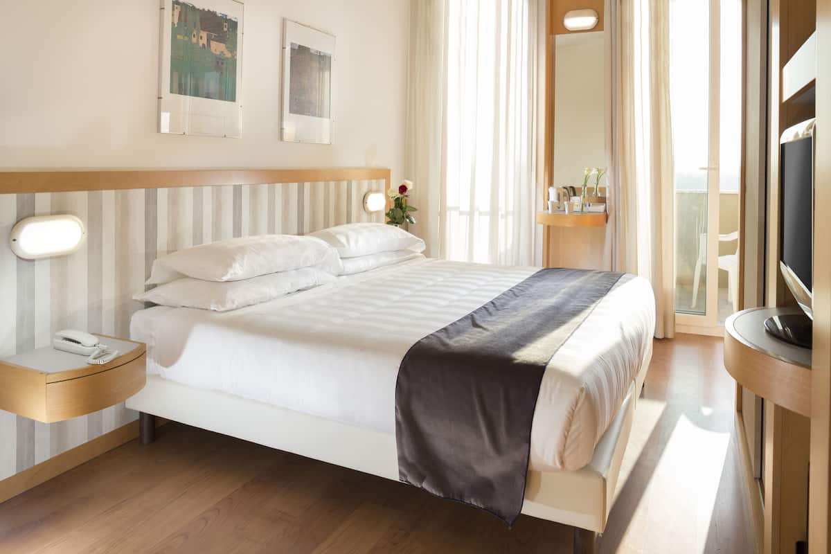 A hotel room with a bed, bedside tables, a TV, and a window with curtains.