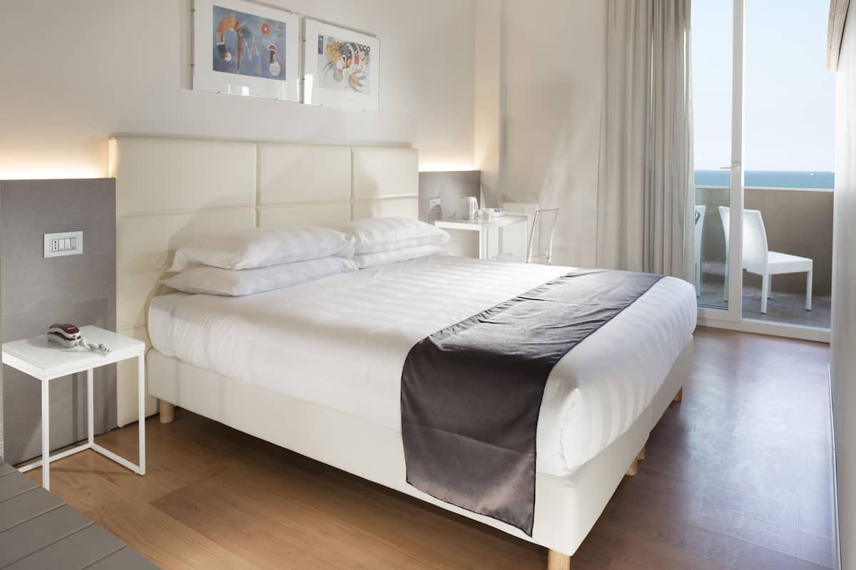 A modern hotel room with a large bed, bedside tables, a small desk, and a balcony with a view.