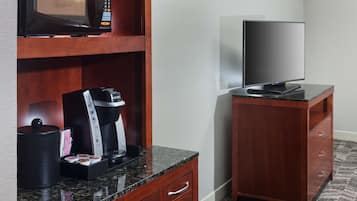 A hotel room with a kitchenette area including a microwave, coffee maker, and a flat-screen TV on a cabinet.