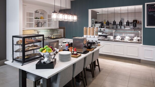 Una cocina moderna con un sistema tipo bufé, que incluye una vitrina con pasteles, una máquina de café y varios recipientes de comida.