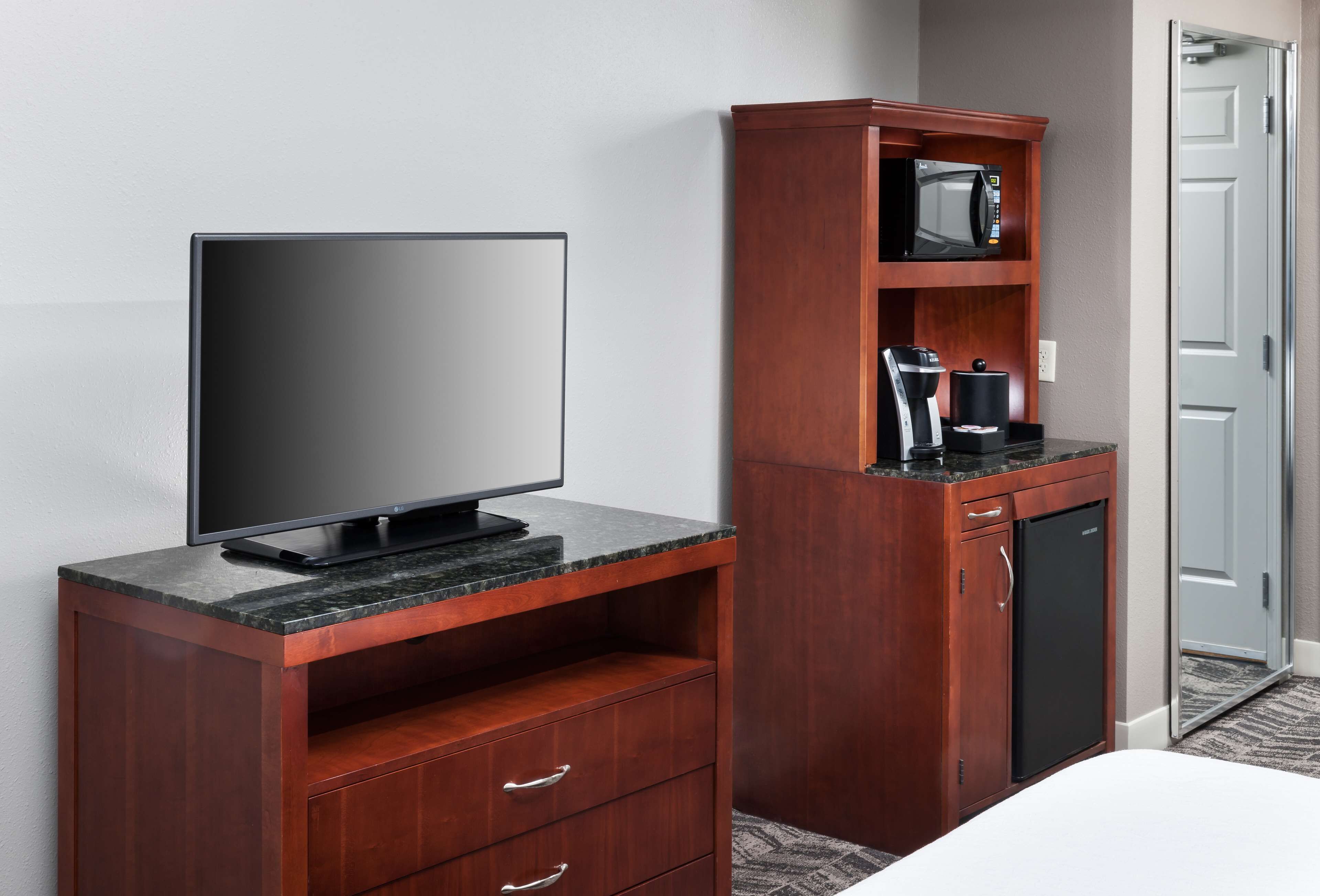 A hotel room with a flat-screen TV on a wooden cabinet, a microwave, and a coffee maker on a wooden shelf.