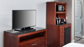 A hotel room with a flat-screen TV on a wooden cabinet, a microwave, and a coffee maker on a wooden shelf.