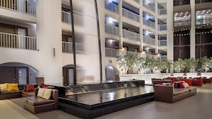 Vestíbulo de hotel de varios niveles con una fuente central, zonas de estar y balcones.