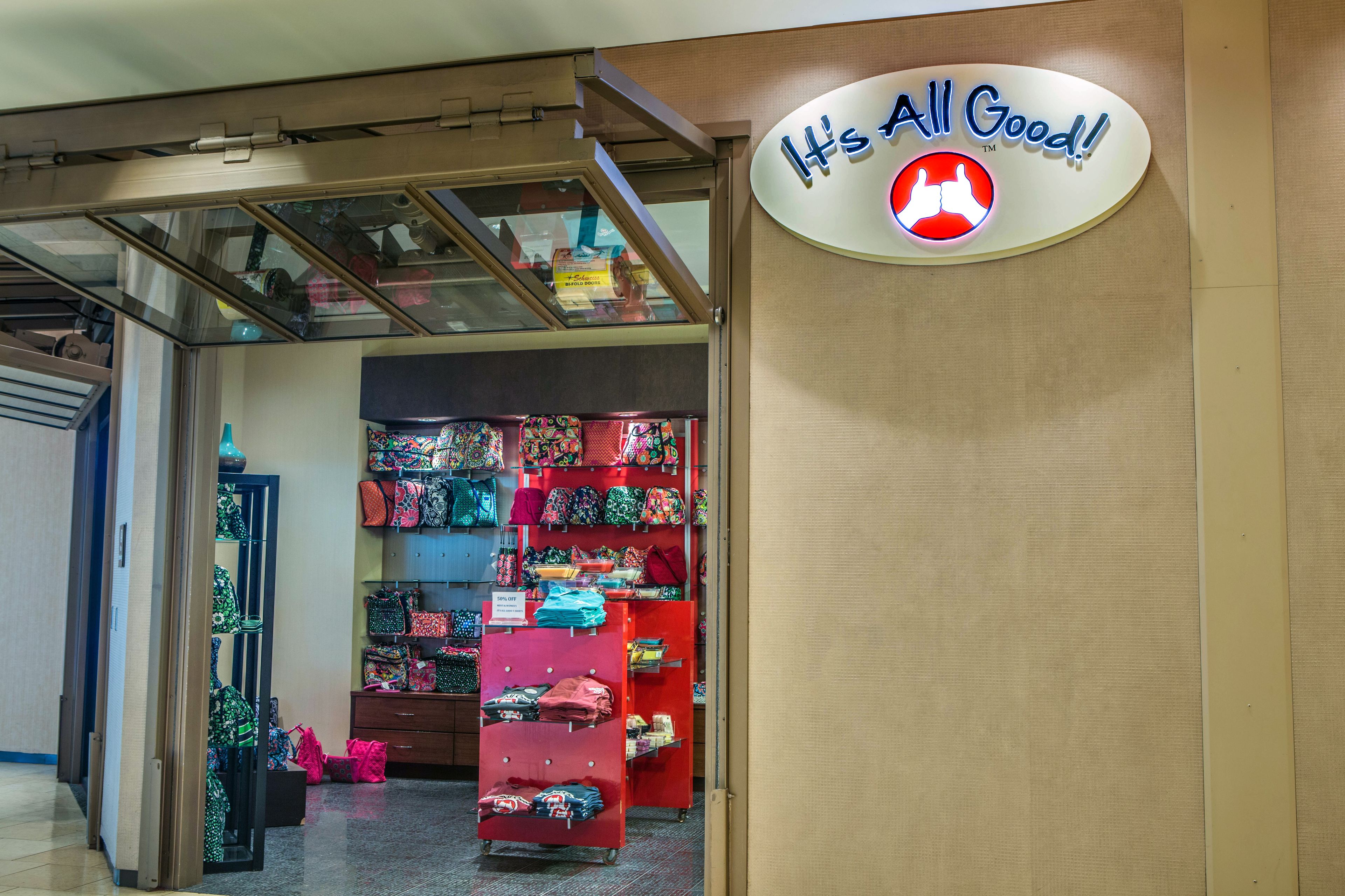 A store with a sign that says "It's All Good!" and a variety of colorful bags on display.