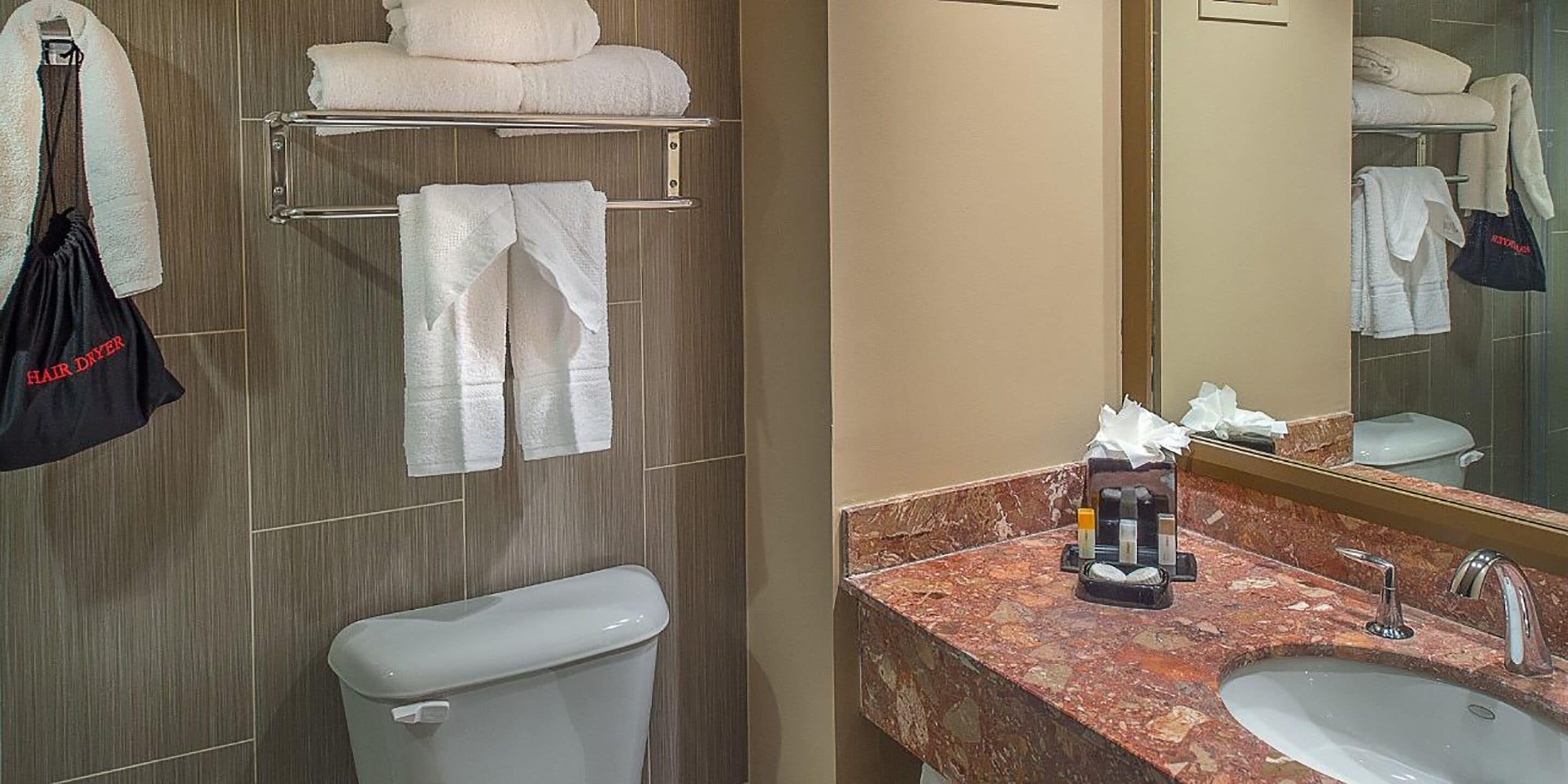 A bathroom with a toilet, a sink with a marble countertop, and towels hanging on a rack.