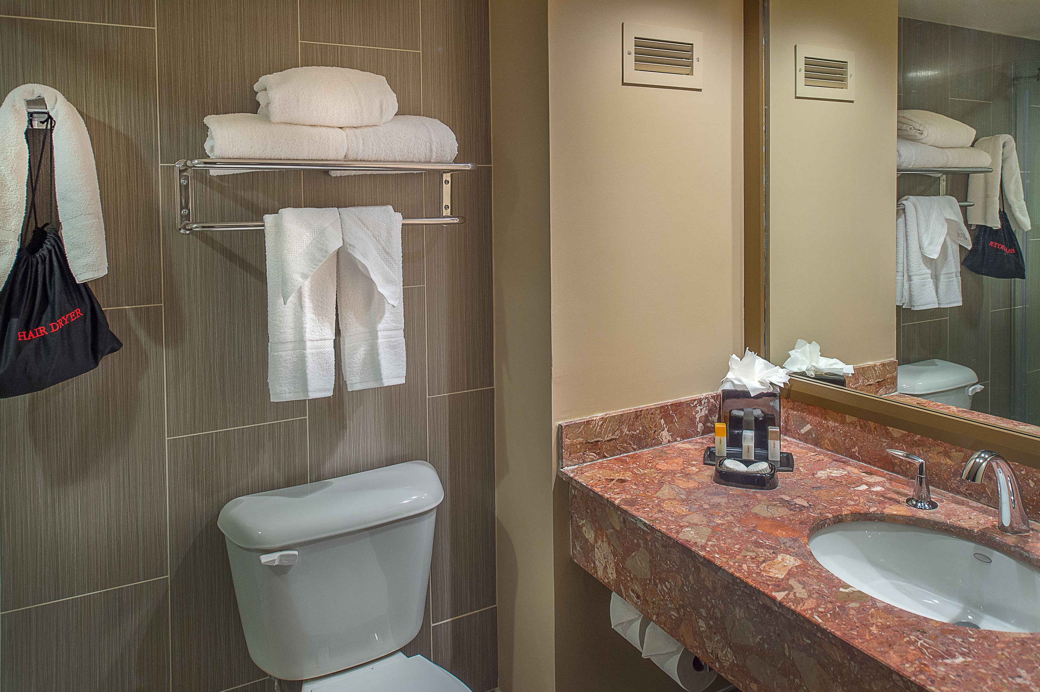 A bathroom with a toilet, a sink, a towel rack with folded towels, and a mirror.