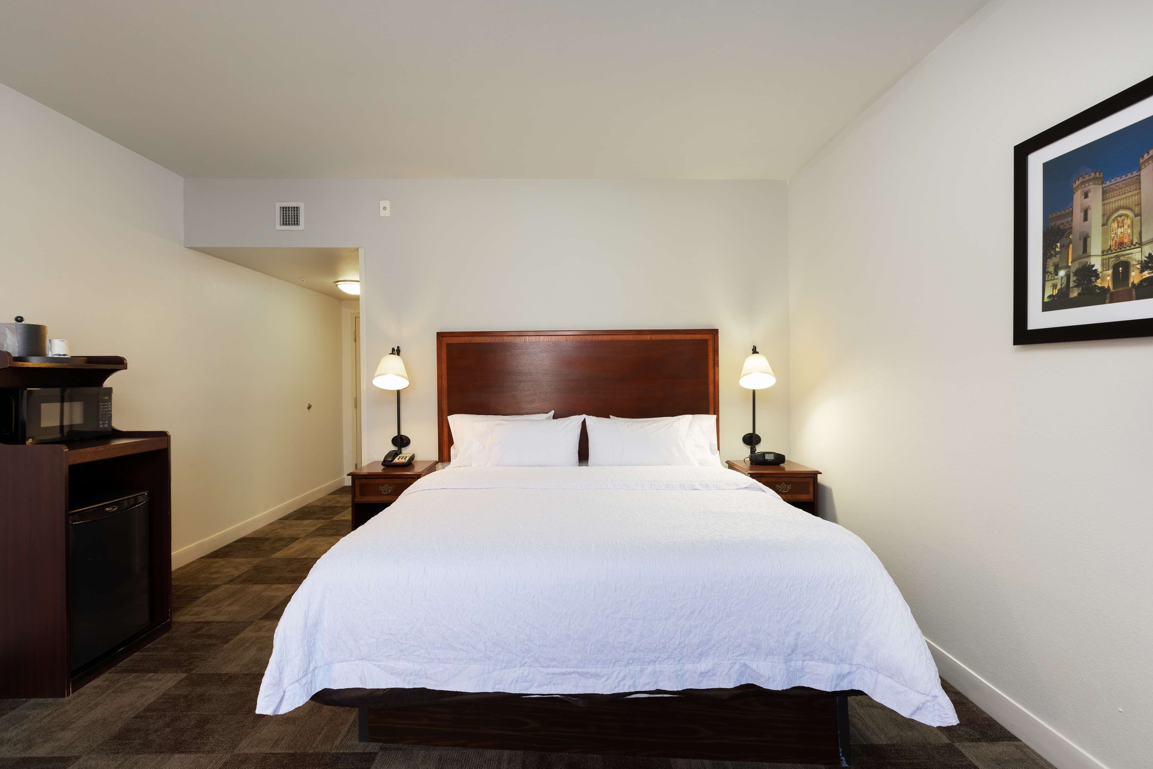 A neatly made bed with white linens, a wooden headboard, and two bedside lamps.