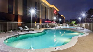 A hotel pool area with lounge chairs, a swimming pool, and a building with a red sign. - Hampton Inn & Suites Baton Rouge - I-10 East (Baton Rouge)