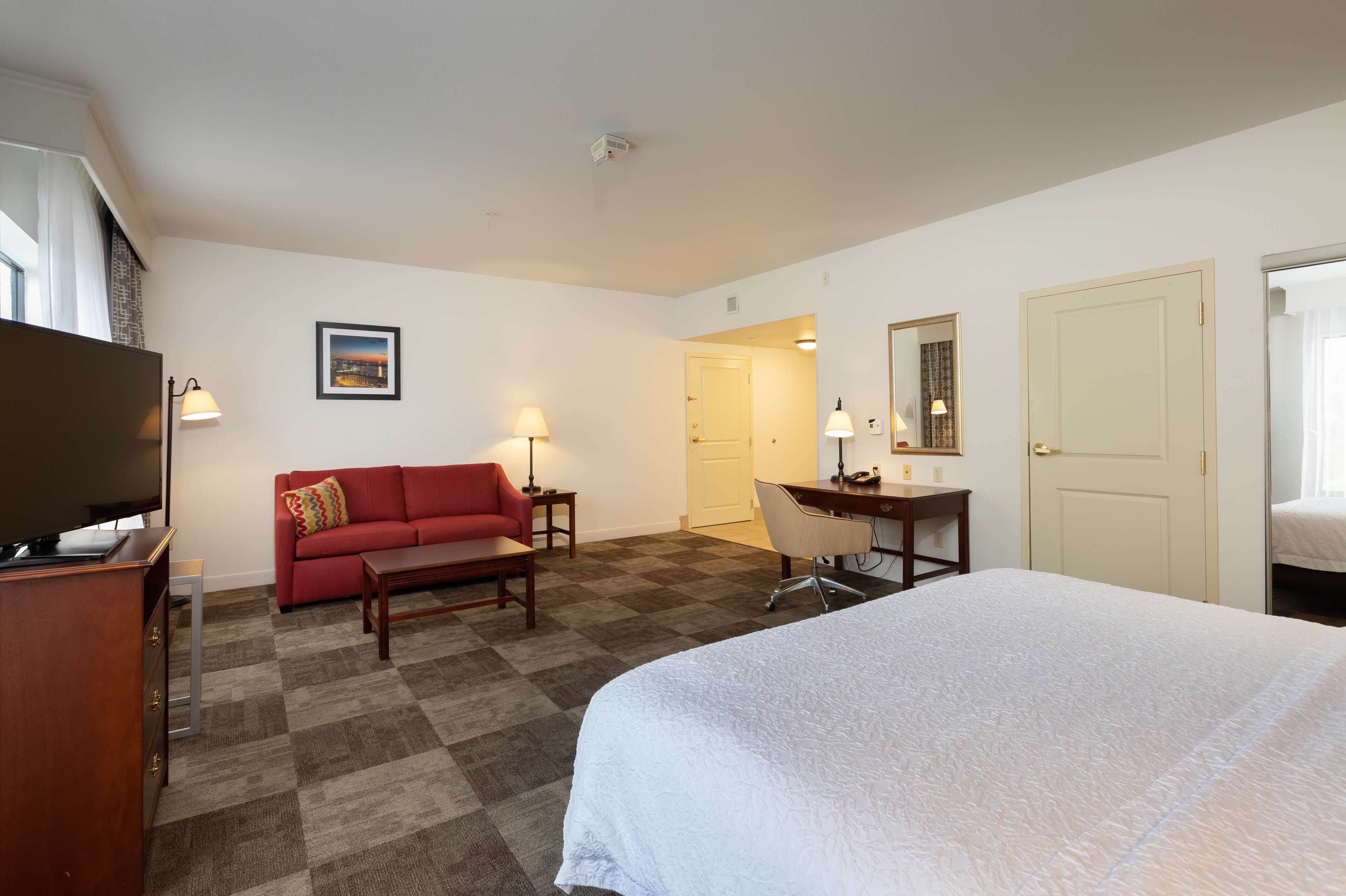 Habitación de hotel con una cama grande, un sofá rojo, un escritorio con una silla, un televisor y un cuadro en la pared.