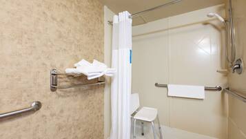 A bathroom with a shower, grab bars, a white chair, and a towel rack.