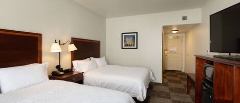 A hotel room with two beds, a desk with a computer, a TV, and a framed picture on the wall.