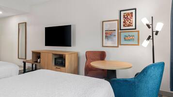 Habitación de hotel con cama, televisor, aparador de madera, mesa redonda y una silla azul.
