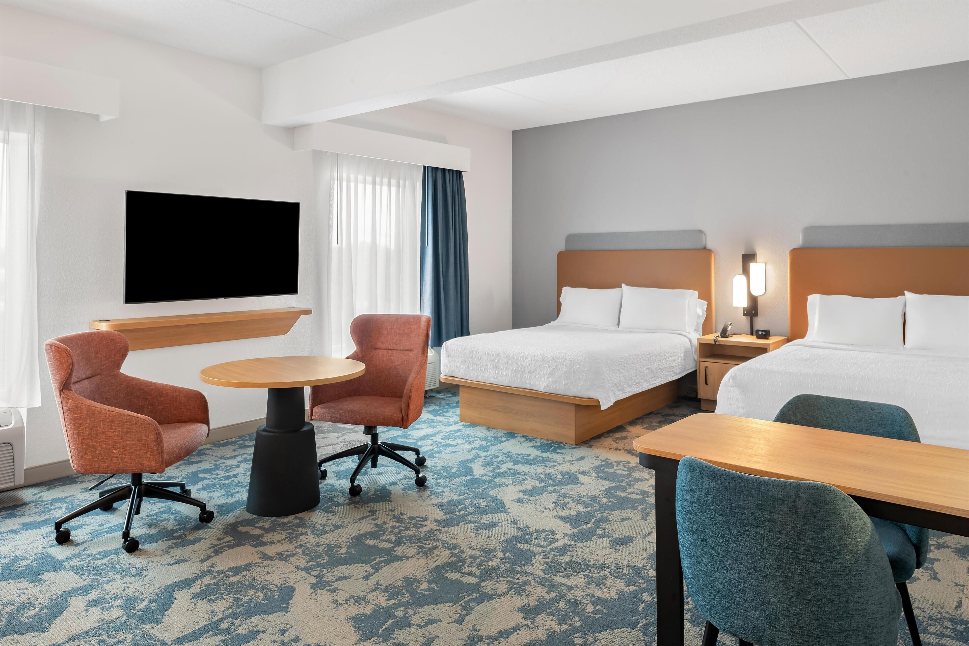 A hotel room with two beds, a TV, a desk, and two chairs.