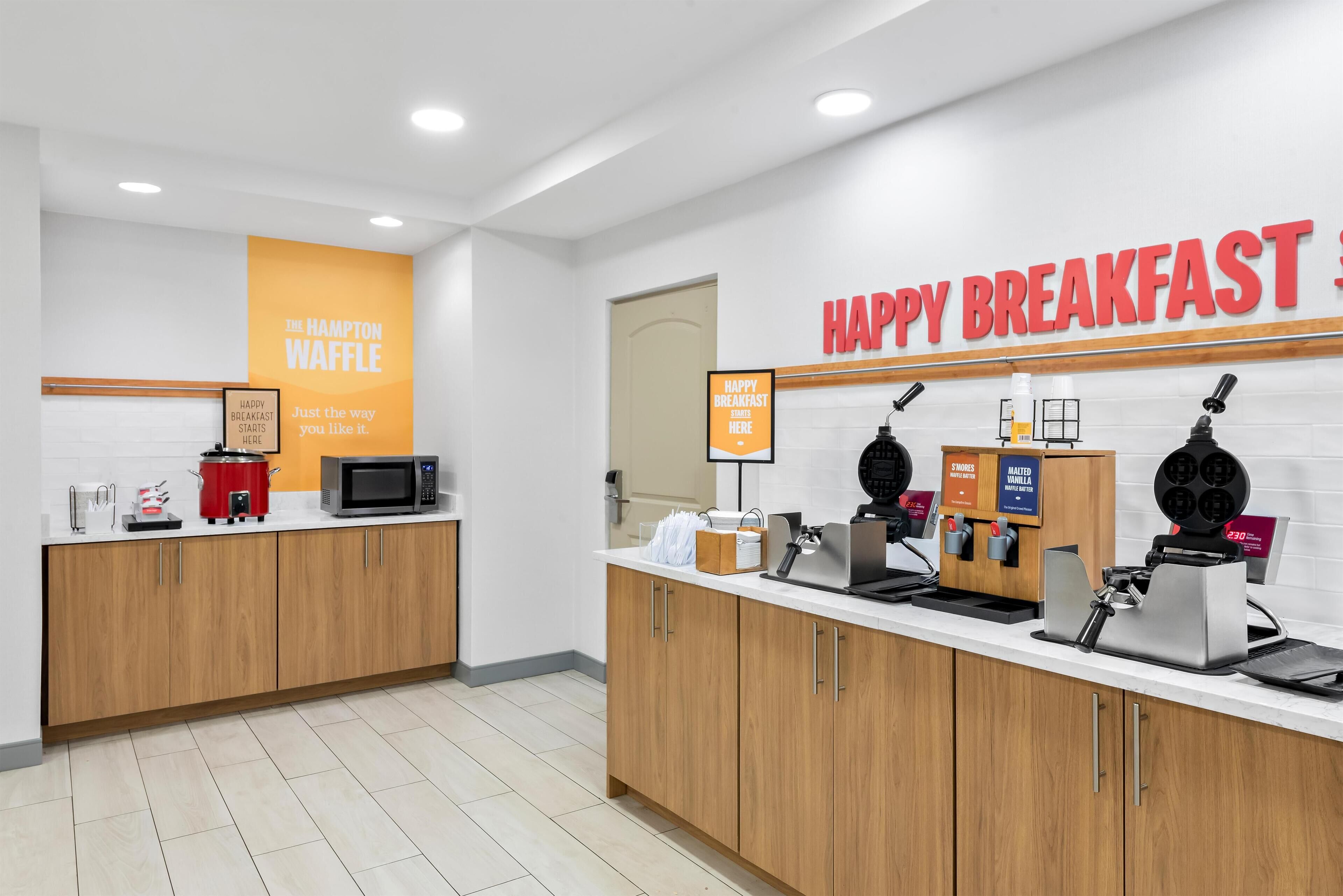 A breakfast area with a sign reading "HAPPY BREAKFAST" and a waffle station.
