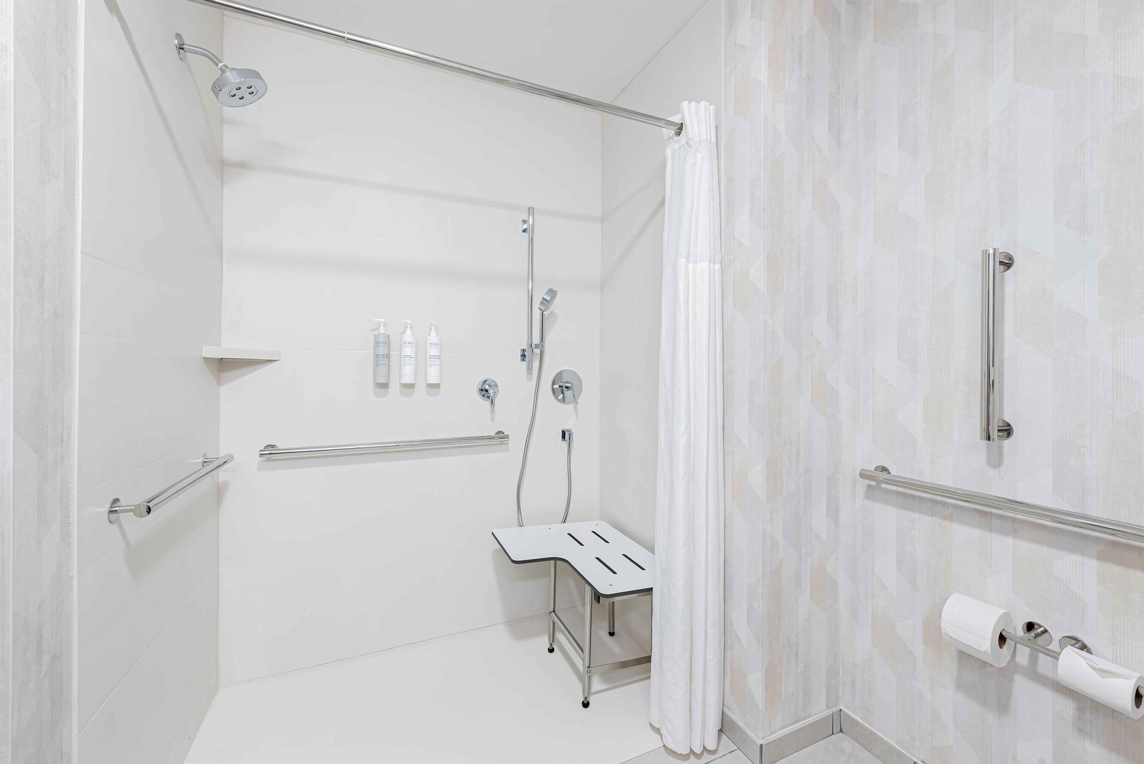 A modern bathroom with a shower, toilet, and handrails.