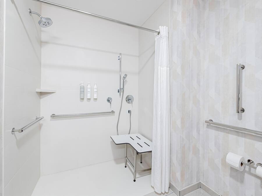 A modern bathroom with a shower, toilet, and handrails.