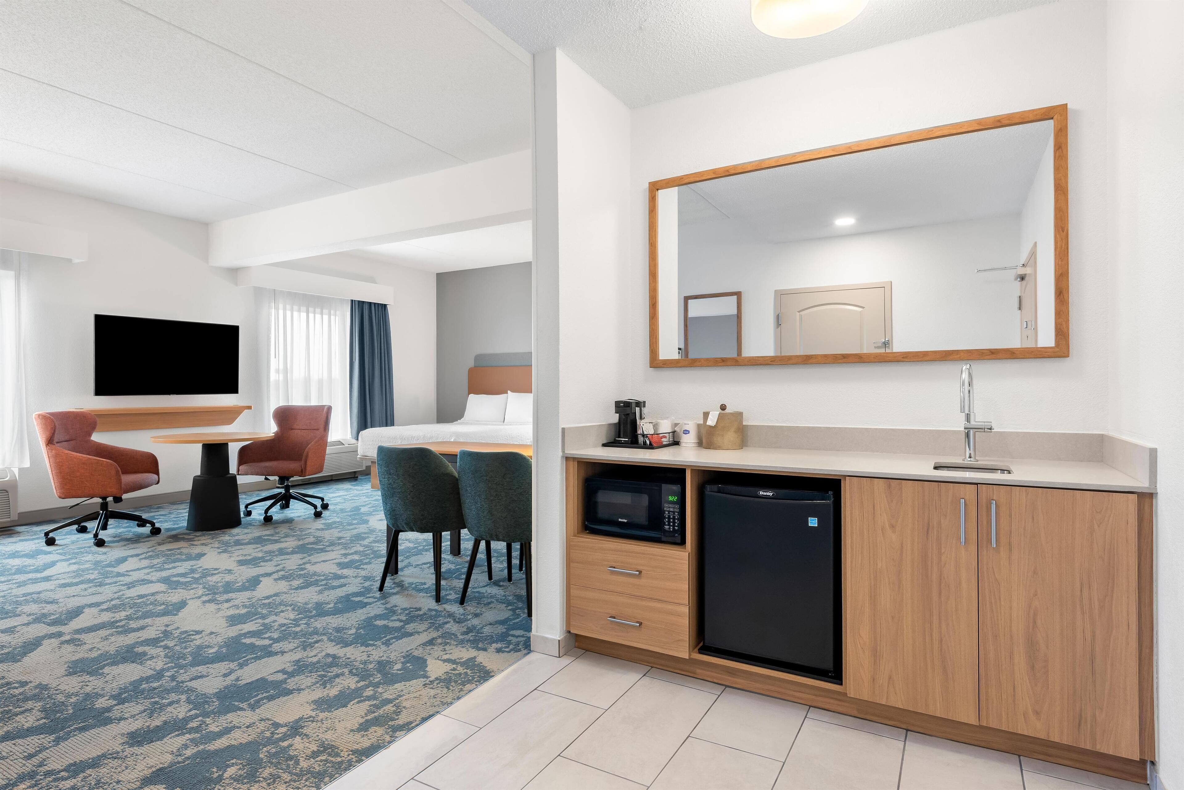 Een hotelkamer met een bed, een bureau, een stoel, een televisie, een spiegel, een wastafel en een magnetron.
