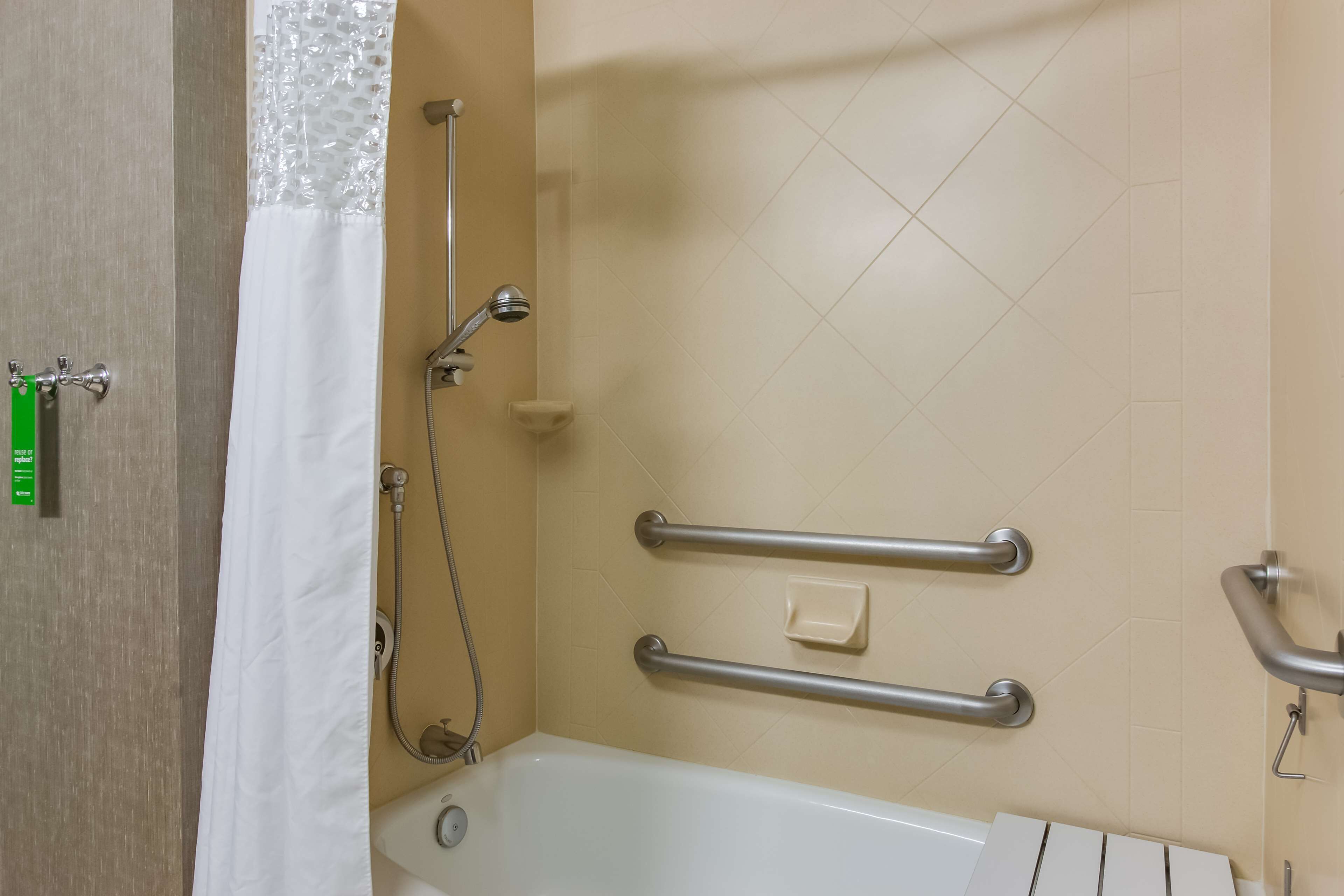 A bathroom with a bathtub, grab bars, a shower head, and a soap dish.