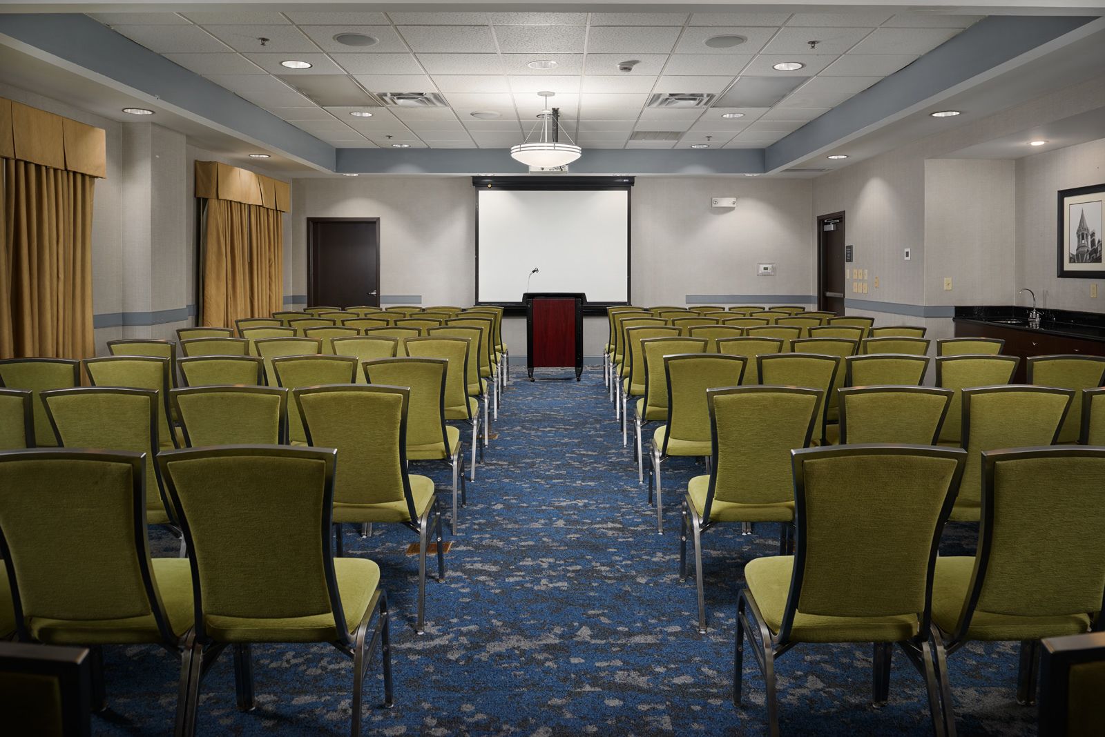 A conference room with rows of green chairs, a podium, and a projector screen.