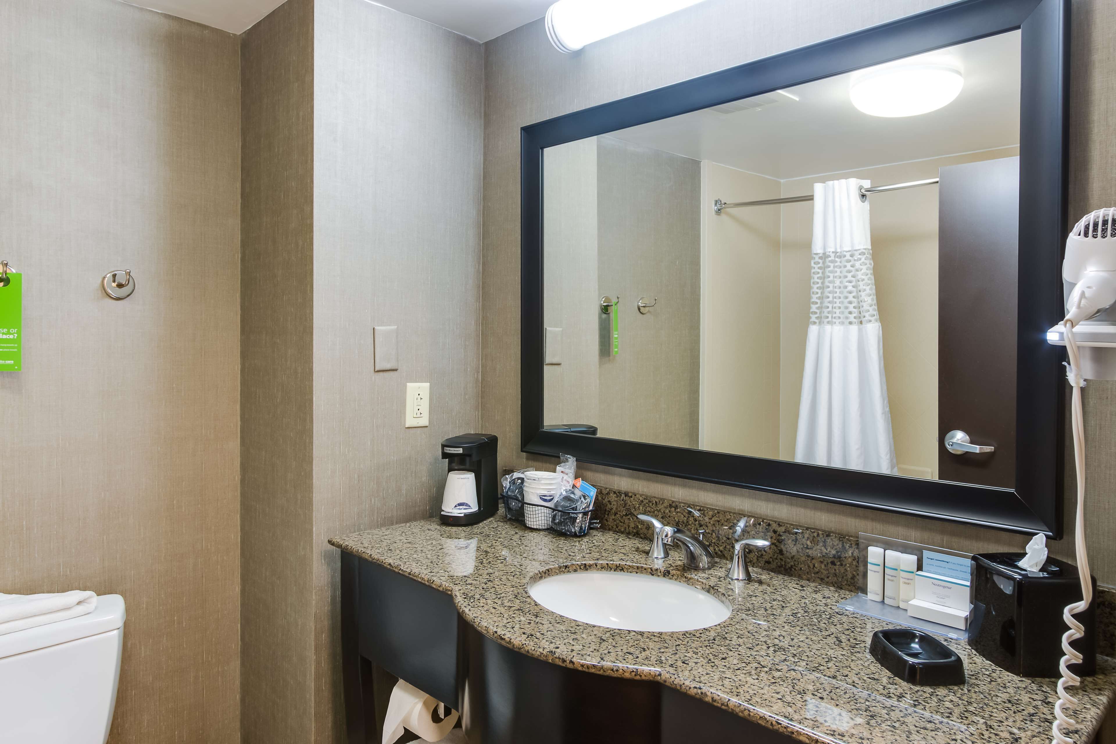 A hotel bathroom with a granite countertop sink, a large mirror, a hairdryer, and a towel rack.