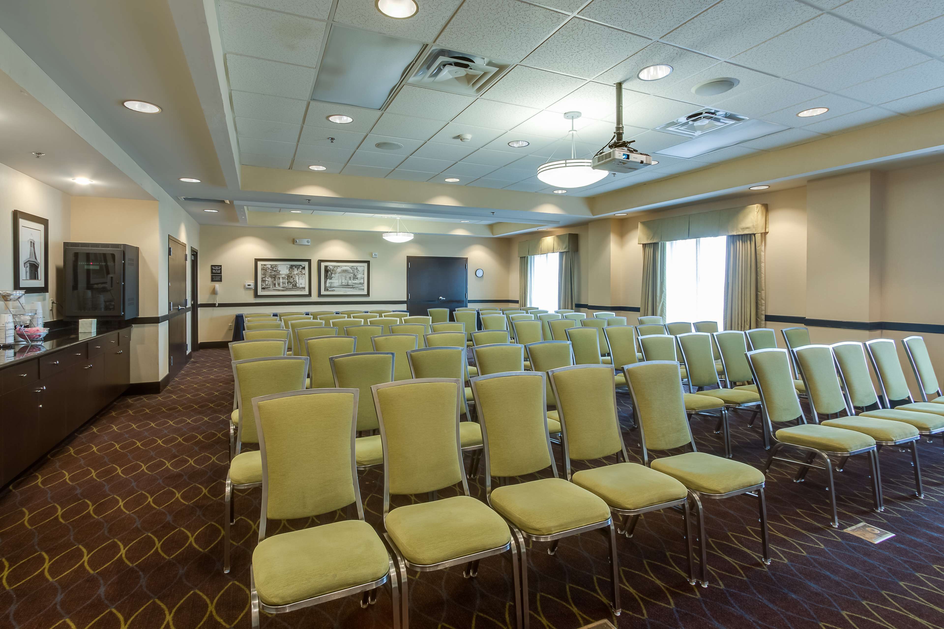 A conference room with rows of chairs, a projector, and a large window with curtains.