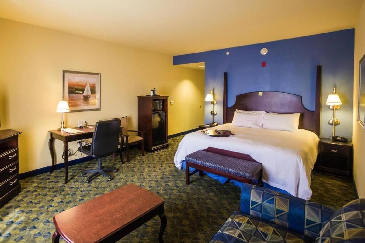 A hotel room with a bed, desk, chair, and a bench.