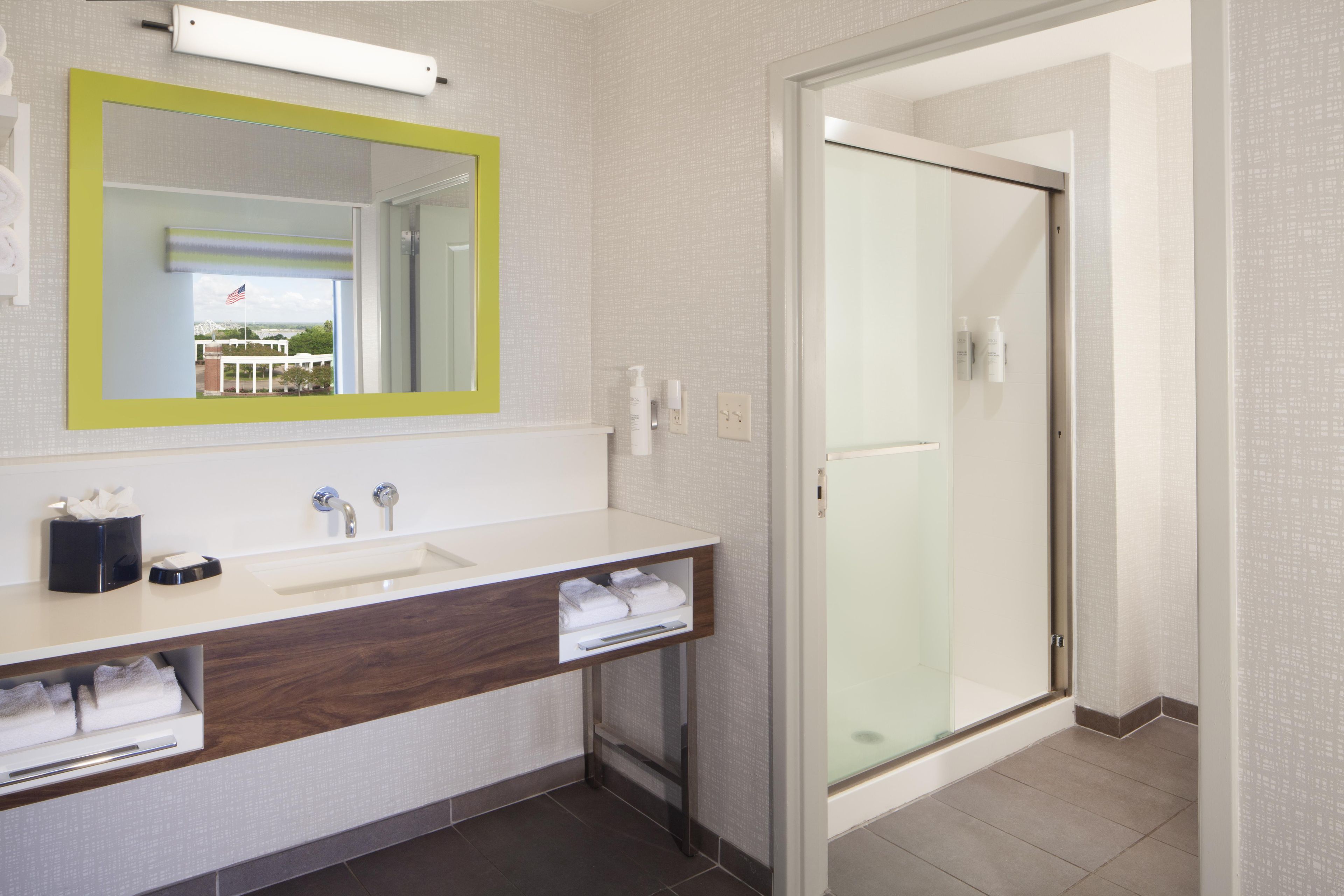 Un baño moderno con un espejo grande, dos lavamanos, una ducha y vistas a un edificio.