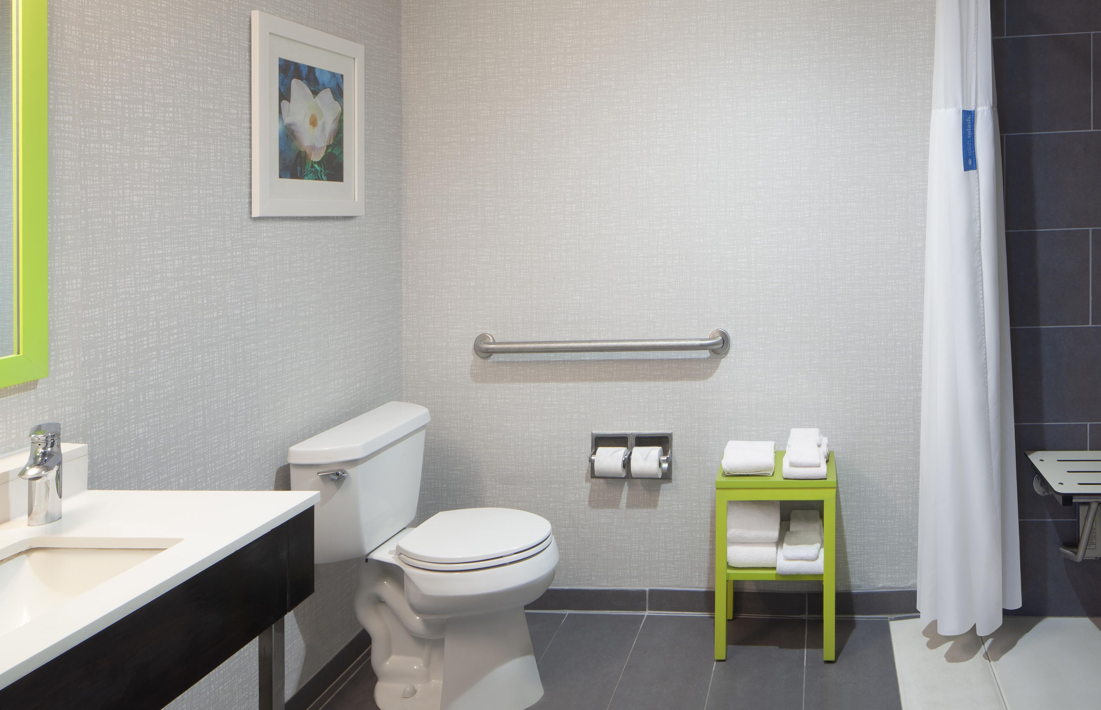 Un baño con inodoro, barra de apoyo, toallero y lavamanos.