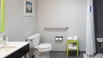 Un baño con inodoro, barra de apoyo, toallero y lavamanos.