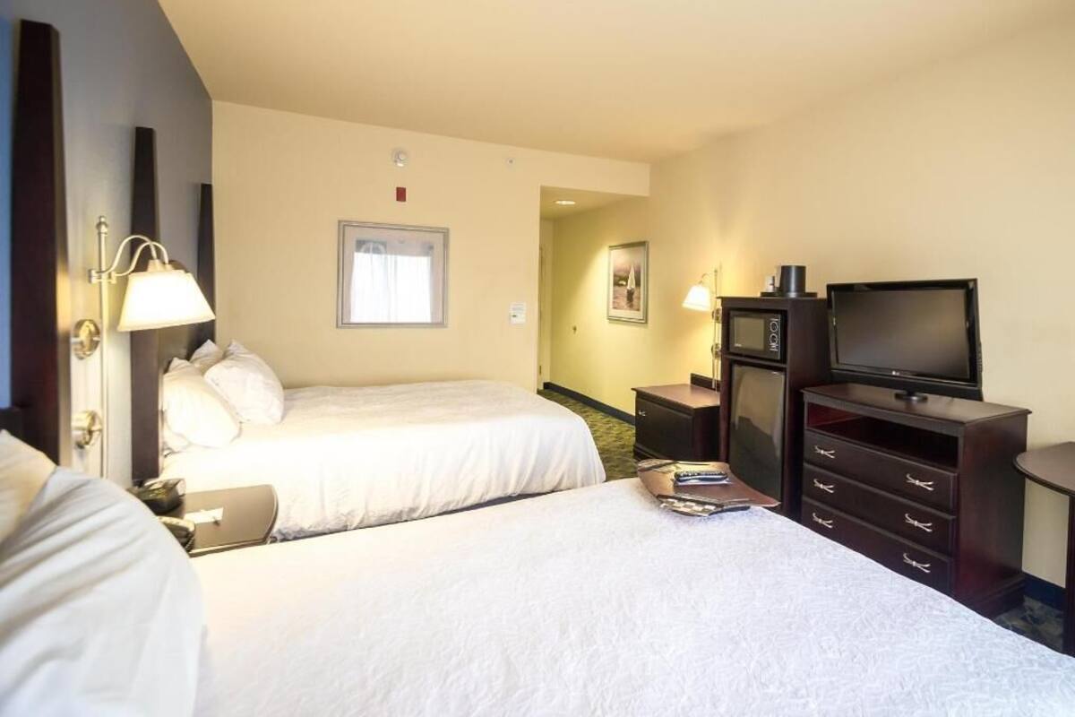 A hotel room with two beds, a television, a desk, and a microwave.
