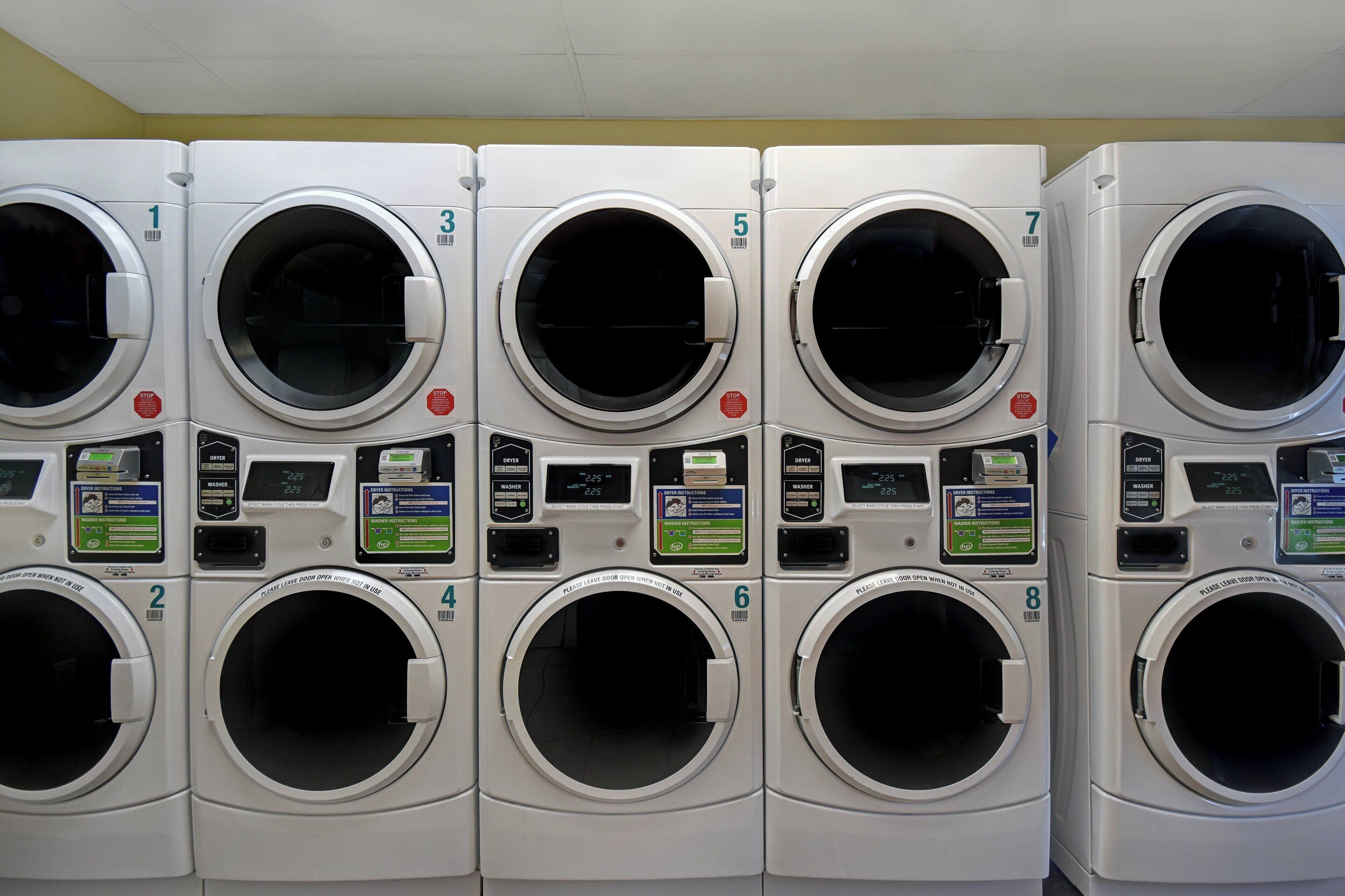 A row of eight white front-loading washing machines with digital displays and control panels, numbered from 1 to 8.