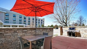An outdoor patio with a table and chairs, a red umbrella, and a stone wall.