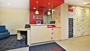 A hotel reception desk with a red accent wall, a map on the wall, and a blue sofa in the background.