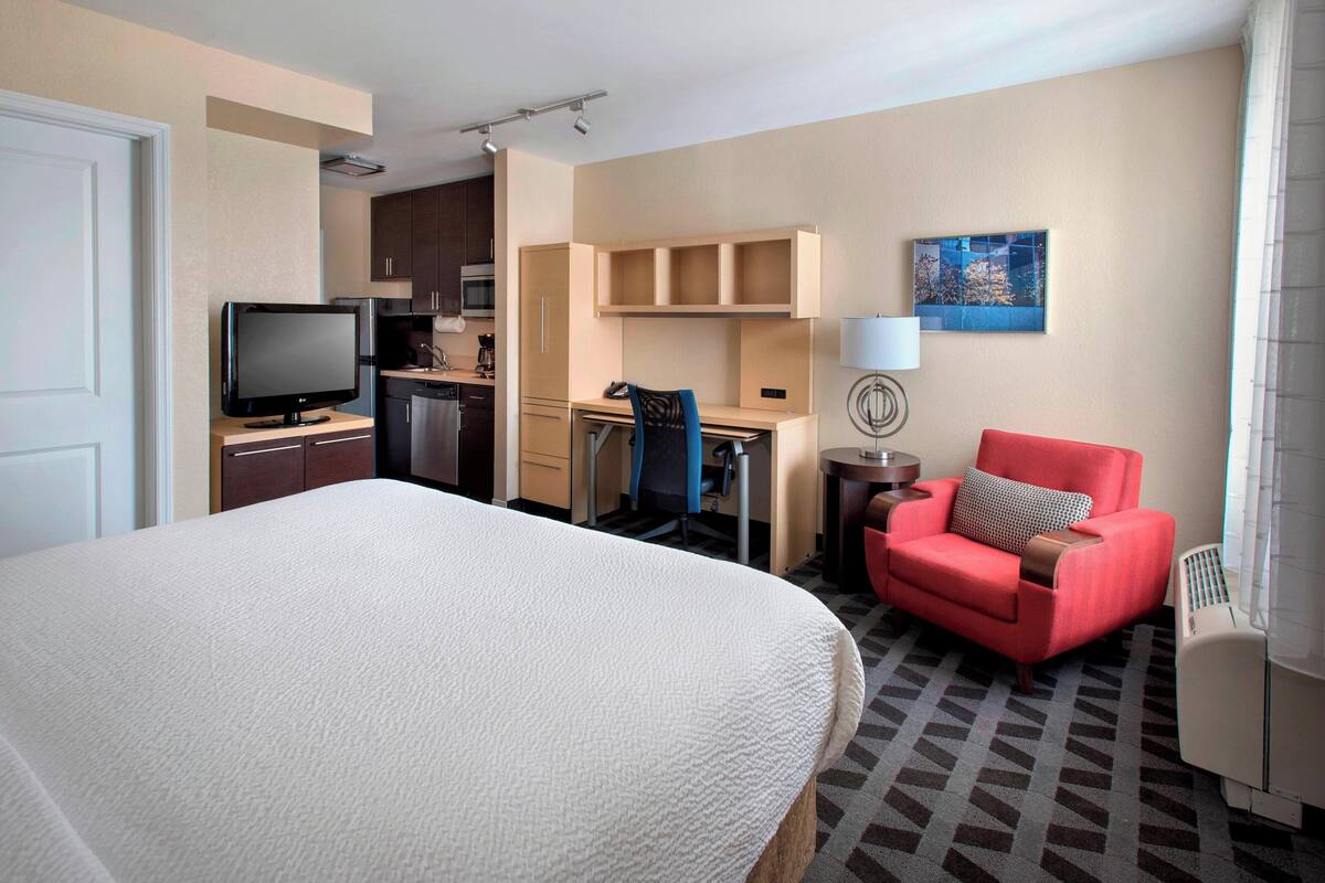 Ein Hotelzimmer mit einem Bett, einem Schreibtisch, einem Sessel, einem Fernseher und einer Küchenzeile.