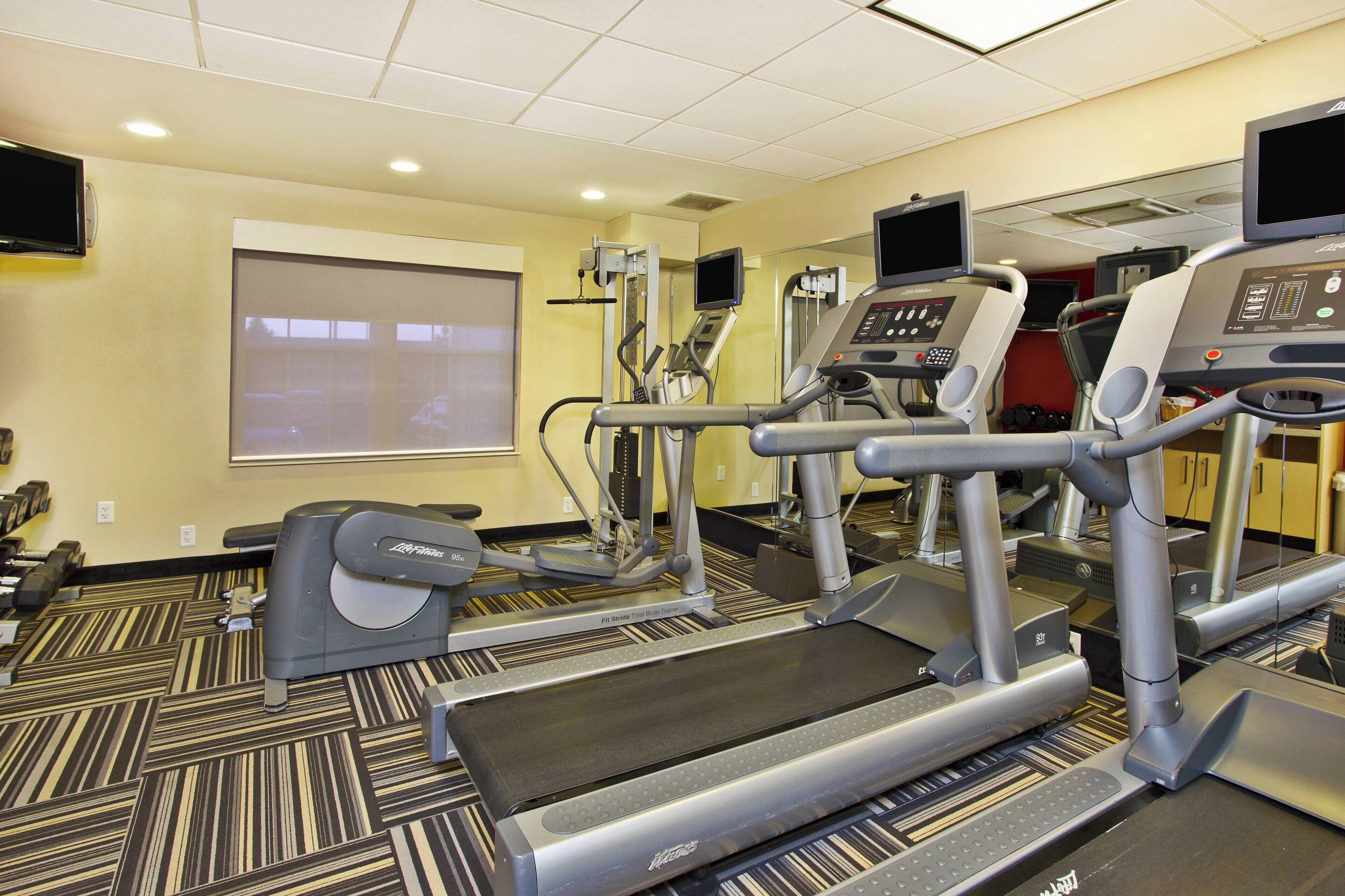 Centro de fitness com esteiras, elípticos e uma tela de projeção na parede.